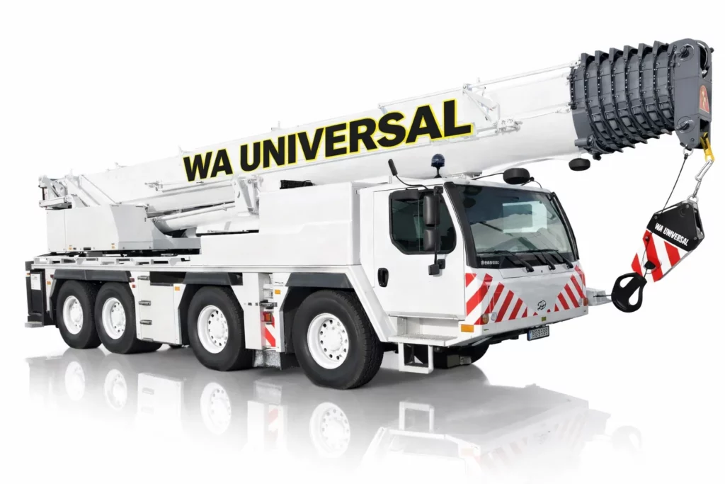 A white mobile crane truck with eight wheels has "WA UNIVERSAL" written on its extended boom. The crane features red and white safety markings on its body and hook.